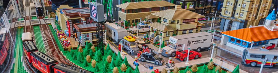 Train tracks running alongside a LEGO town centre, with businesses and a car park